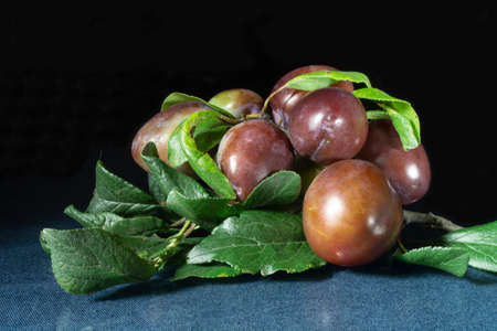 The Ripe plum with green sheet on black background. Green branch with fruit on glass tableの写真素材