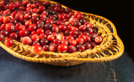 The Ripe red cranberry in braided plate on table. Harvest of the berries on black backgroundの写真素材