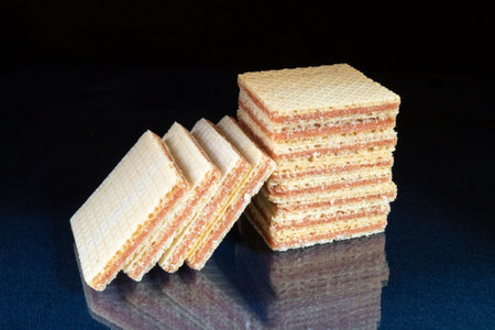 Tasty wafer rests upon glass table with reflection. Sweet products of the feeding on black...