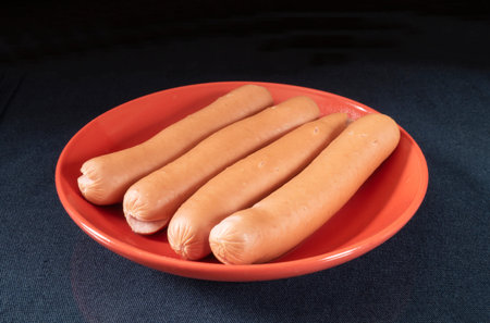 The Hot dogs on table in red plate on black background. The Products of the meat feeding.