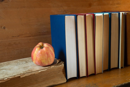 The Red apple with book rests upon wooden regiment. The Subjects close-up.