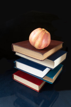 The Book and apple rests upon glass table. Subjects with reflection on black backgroundの写真素材