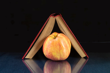 The Book and apple rests upon glass table. Subjects with reflection on black backgroundの写真素材