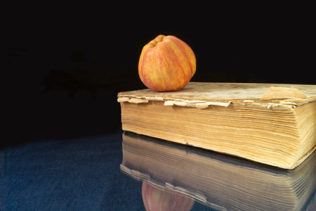 The Book and apple rests upon glass table. Subjects with reflection on black backgroundの写真素材