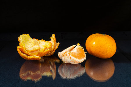 The Segments of the tangerine on glass table with reflection. Products of the feeding on black backgroundの写真素材