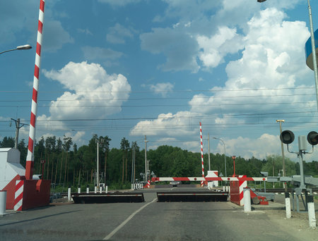 A barrier at a railway crossing in rural areas. Paved road on the background of the sky with clouds