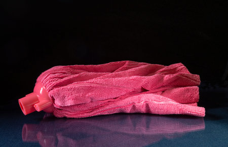 A pink microfiber mop head on a glass table. Household items with reflection on a black background