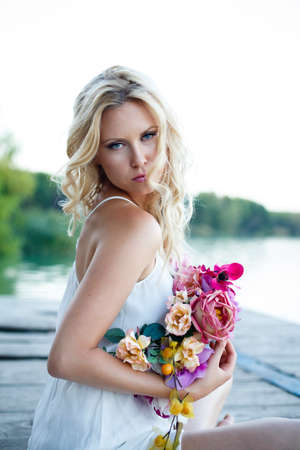 portrait of young beautiful blond female with blue eyes and wavy long hair. Slavic woman wearing romantic white dress and colourfull flower hairbandの写真素材