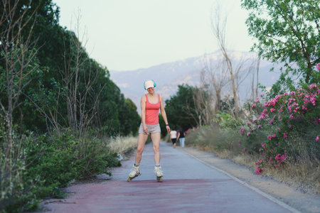 Young woman having fun while roller skating outdoors during sunset. Attractive female wearing a pale...