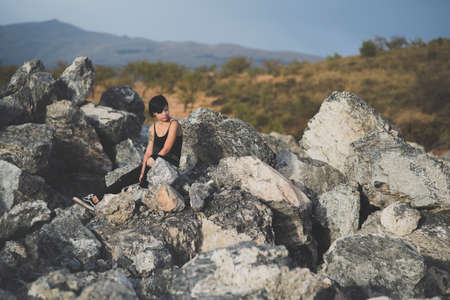 Beautiful young woman wearing black clothes and short haircut sitting on the rocks outdoors. Caucasian brunette girl thinking relaxed with closed eyes in the countryside.の写真素材