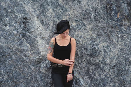 Caucasian young woman and black clothes in a serene pose with closed eyes. portrait of an beautiful brunette girl leaning aginst rock wall.の写真素材