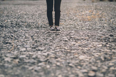 photo of the legs of a lonely young woman dressed in jeans and black sneakers standing on a stone floor in the countrysideの写真素材
