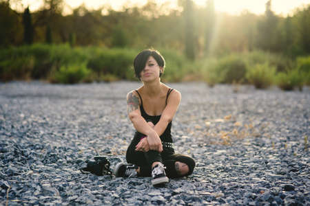 Beautiful young photographer woman wearing black clothes and short haircut sitting on the stone floor outdoors. Caucasian brunette girl thinking relaxed in the countryside.の写真素材