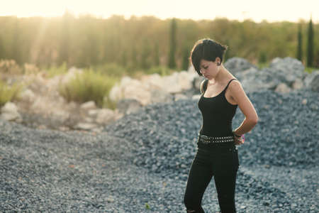 Caucasian  brunette girl with short haircut enjoying her free time outdoors with stone texture background.  Portrait of beautiful young woman with short haircut and closed eyes wearing black clothes.の写真素材