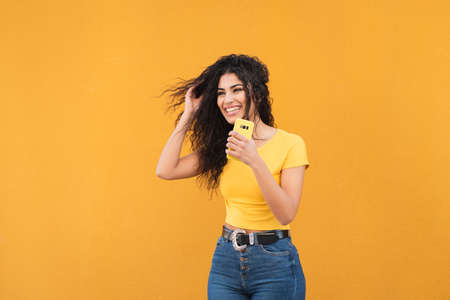 Attractive girl smilling holding her mobile with yellow backgroundの写真素材