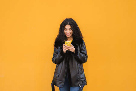 Mixed race girl texting with her mobile with yellow backgroundの写真素材