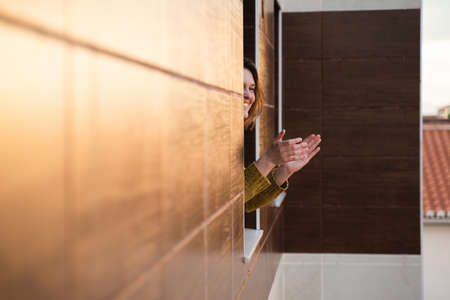 Young woman on quarantine applauding to support health workersの写真素材
