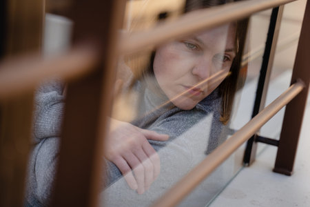 Woman looking melancholy through the glass to the street