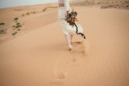 bride walking on sand dune holding flowers bouquetの写真素材