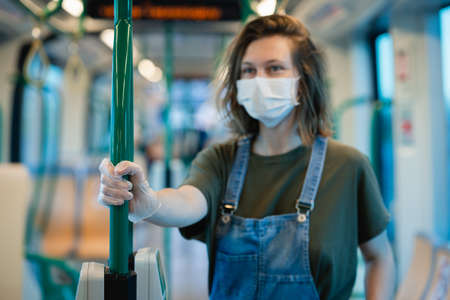 Woman wearing surgical protective mask and gloves in a public transportationの写真素材