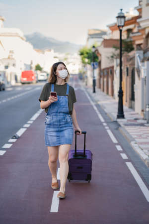 traveller with protection mask against coronavirus visiting the city with her suitcaseの写真素材