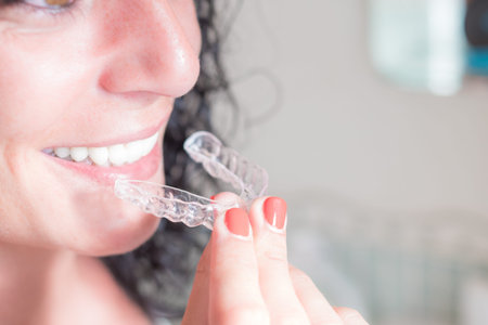 closeup of the face and hand of a young curly haired brunette woman smiling putting on her invisible...