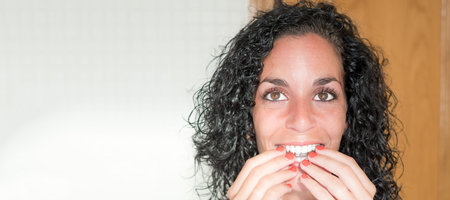portrait of a young curly haired brunette woman smiling putting on her invisible silicone aligner...
