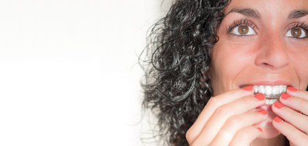 portrait of a young woman smiling putting on her invisible silicone aligner for dental correction....