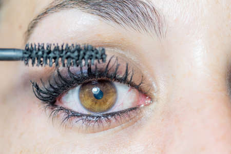 Close-up of the eye of a young woman putting on makeup with mascara for her eyelashesの写真素材
