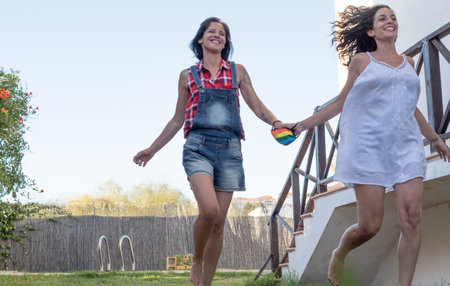 couple of women. Girlfriends having fun and laughing as they run through the garden of a chalet on...