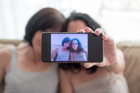 two young women friends have fun and laugh while taking a selfie with their phonesの写真素材