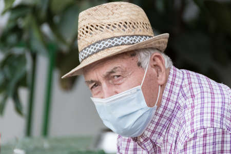 Elderly man with straw hat wearing a face protection mask due to the global pandemic of coronavirus, covid 19.の写真素材