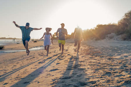 young friends playing and having fun while running and jumping on the beach on vacation. summer activity. friendship, fun and unity conceptの写真素材