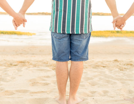 young man in shorts and striped shirt holding hands with his friends in front of the beach. friendship, travel and leisure conceptの写真素材