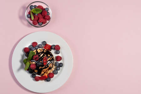 top view of homemade American pancakes with fresh blueberries, raspberries, strawberries and chocolate syrup. Healthy breakfast in the morning. Pink backgroundの写真素材