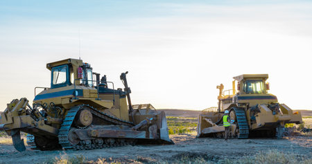 heavy machinery. construction worker with helmet and protective vest next to excavator and large...