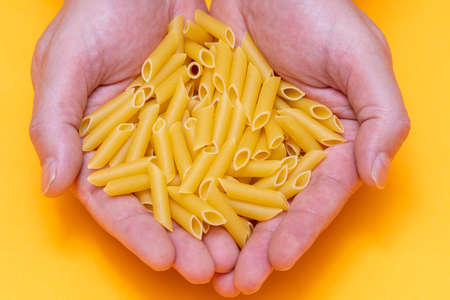 A person's hands holding a handful of macaroni on orange background. healthy eating and life conceptの写真素材