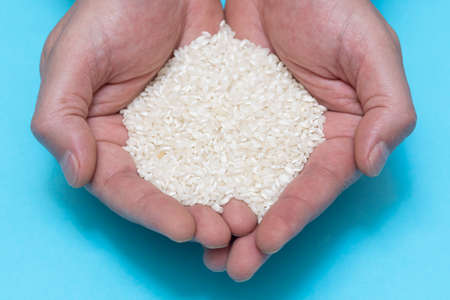 A person's hands holding a handful of rice on blue background. food, cooking and healthy eating conceptの写真素材