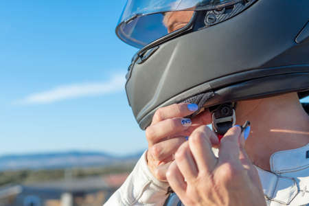 young female biker fastening her safety helmet to ride a motorcycle. safety and protection concept on the roadの写真素材
