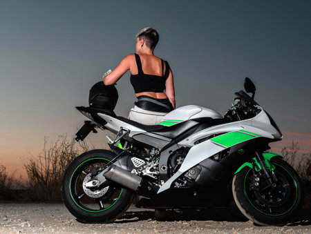 biker woman with short blond hair on her back leaning on her road motorcycle with her safety helmet...