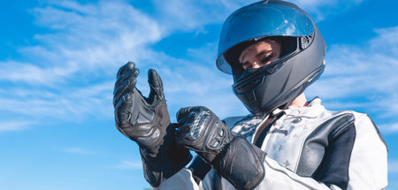 woman dressed as a biker with black safety helmet putting on her leather gloves getting ready to...