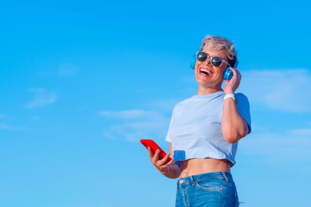 young pretty blonde woman with short hair and sunglasses laughing while listening to music with...