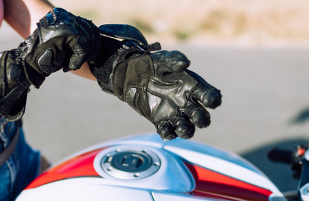 detail of the hand of a young biker woman putting on her leather protection gloves to ride a...