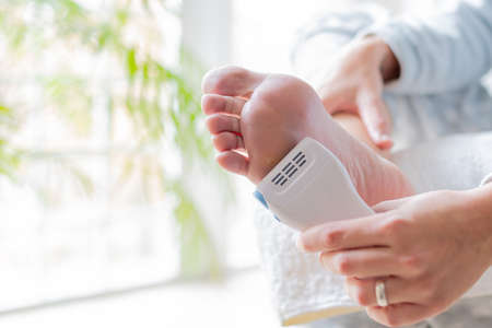 hands of a young woman using an electrical device to soften the feet and remove calluses. body care and pedicure conceptの写真素材