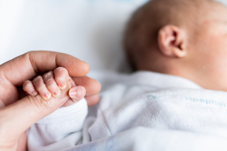 hand of a father holding the small hand of his newborn daughter in the maternity hospital. family concept, baby care and maternal and paternal loveの写真素材