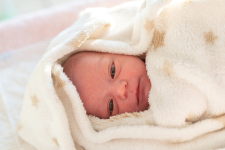 portrait of a newborn baby lying in his crib wrapped in a soft white blanket with stars ready to go...