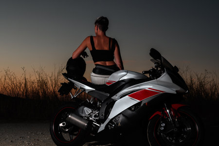 young biker woman with short hair watching the sunset leaning on her motorcycle after a road tripの写真素材