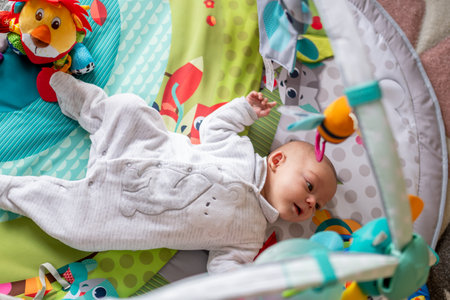 newborn baby lying on her back in a playground, baby gym to stimulate her with figures, toys and colors. concept of early stimulation of the babyの写真素材
