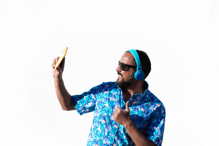 young bearded hipster man dressed in hawaiian shirt, sunglasses and wireless headphones taking a...