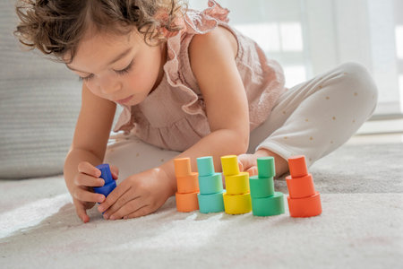 beautiful little girl has fun stacking blocks and pieces of sustainable wood of different colors. montessori material concept of learning and development of skills and motor skills in childhoodの写真素材